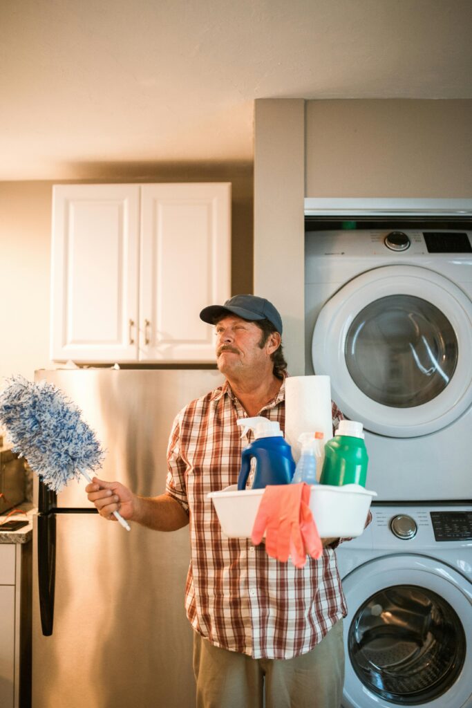pexels-photo-5591963-5591963 Adult man holding cleaning supplies next to washing machine in laundry room.